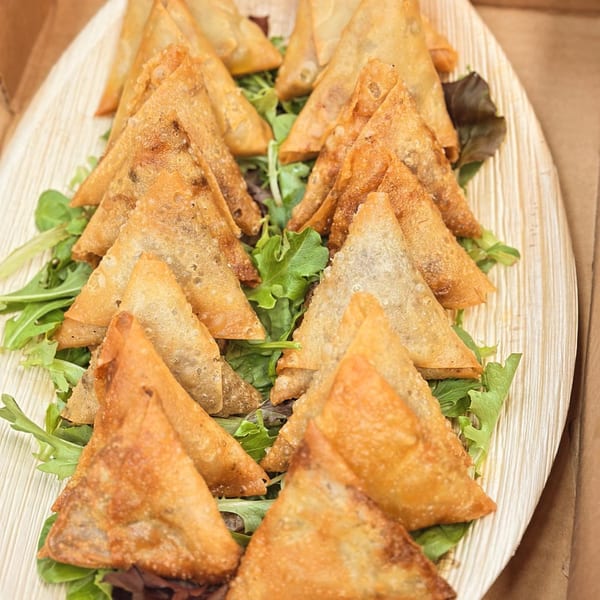 Golden-brown, triangular Middle Eastern pastries, likely sambousek, arranged on a bed of fresh green lettuce.