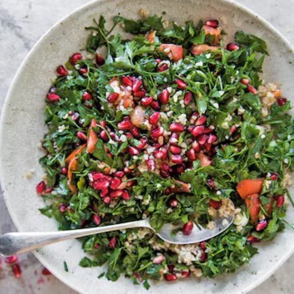 A vibrant tabbouleh salad with fresh parsley, tomatoes, and pomegranate seeds, served in a white bowl.