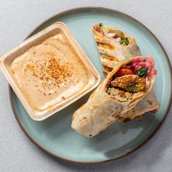 Two falafel wraps with pickled vegetables and a side of tahini sauce on a blue plate.