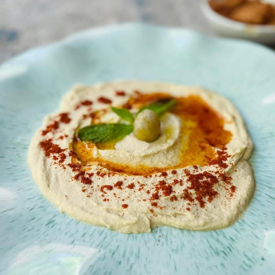 Creamy hummus drizzled with olive oil, sprinkled with paprika, and garnished with an olive and mint.