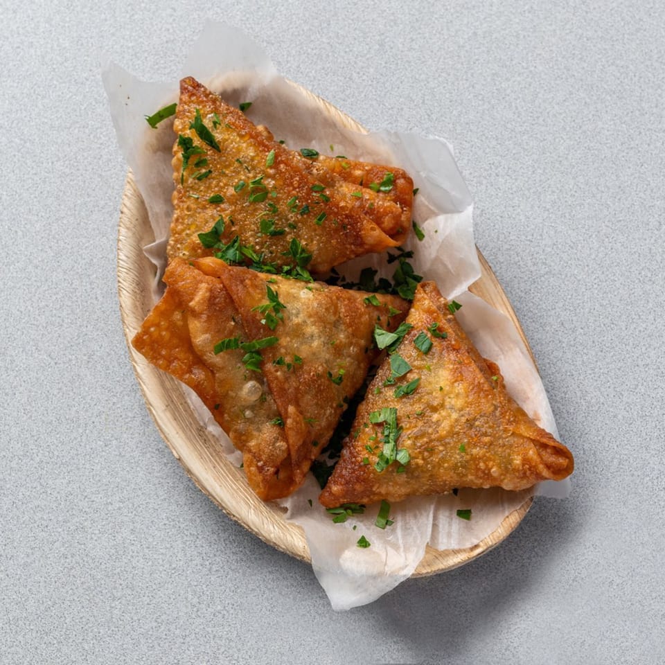 Three golden-brown, triangular samosas, garnished with fresh parsley, served on parchment paper in a wooden dish.