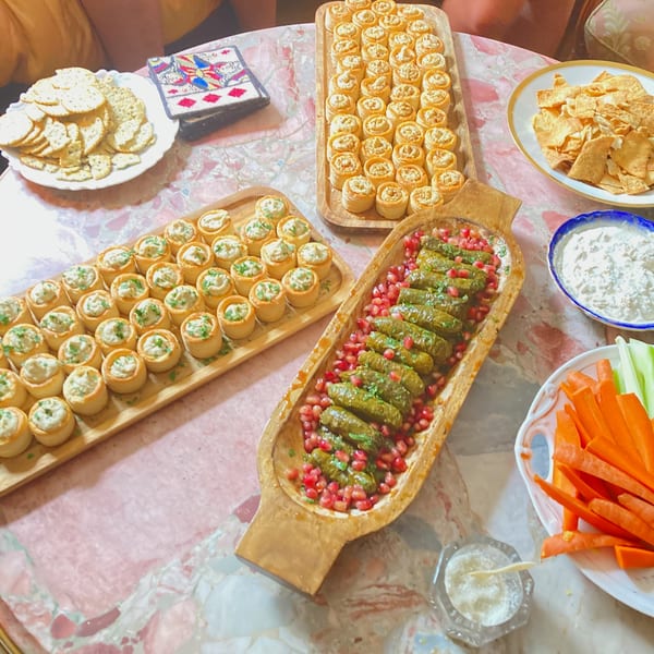 A table laden with appetizers, including stuffed grape leaves, mini tarts, crackers, and vegetable sticks.