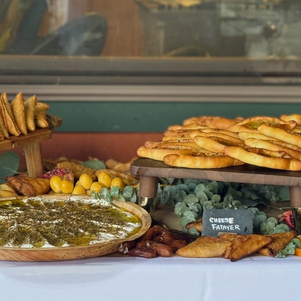 A buffet table laden with Middle Eastern pastries, dips, and dates, including cheese fatayer.