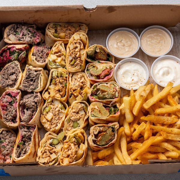 A takeout box filled with various shawarma wraps, fries, and dipping sauces.