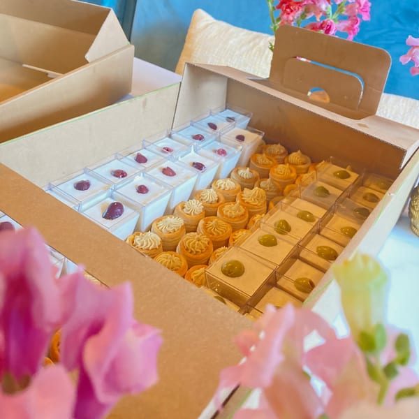 Open catering boxes filled with mini desserts: white puddings with berries, cream-filled pastries, and green-topped desserts.