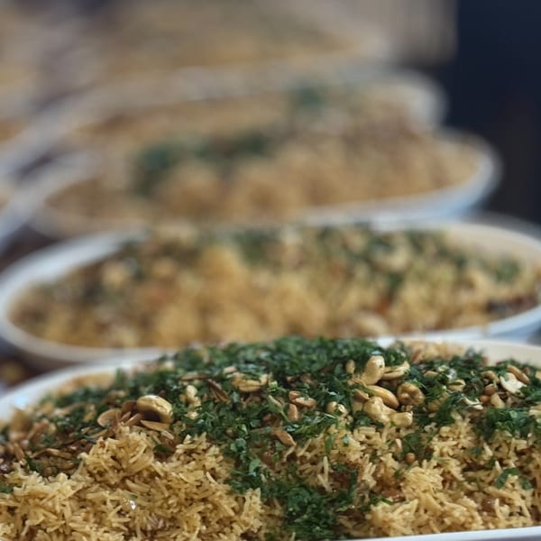Multiple white platters of rice pilaf topped with green herbs and cashews, in a row.