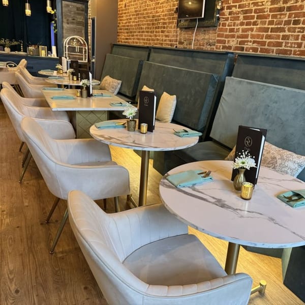 Elegant dining room at Sara's Kitchen with marble tables, plush seating, and brick walls.