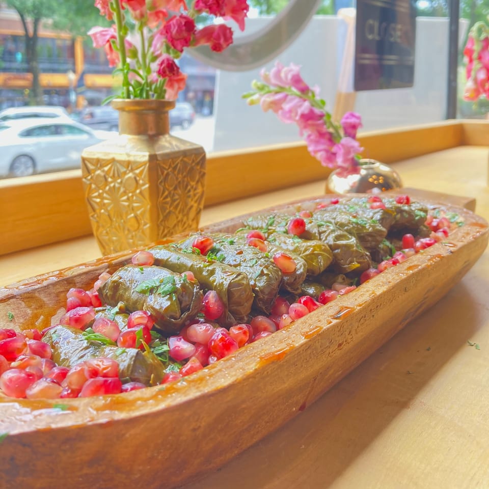 Grape leaves stuffed with rice and herbs, garnished with pomegranate seeds in a wooden dish.