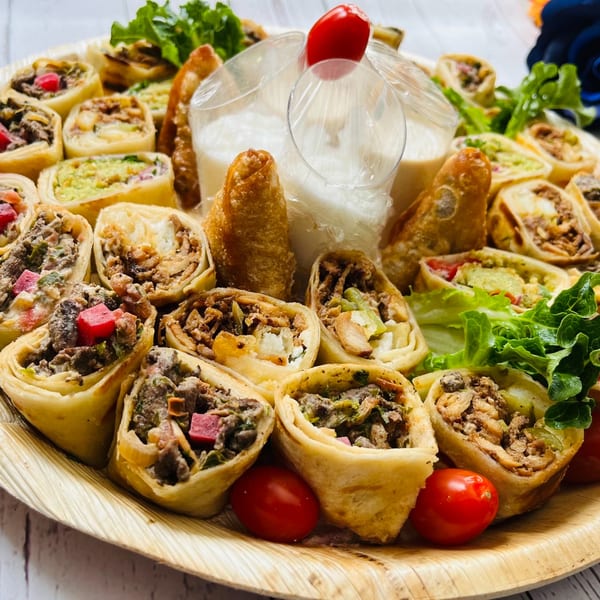 A platter of Middle Eastern wraps and spring rolls with dipping sauce and cherry tomatoes.