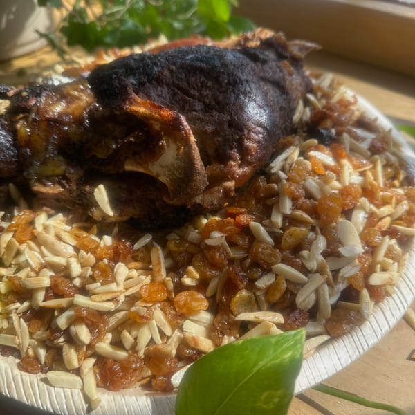 Roasted meat with almonds and golden raisins on a white plate, with green leaves in the foreground.