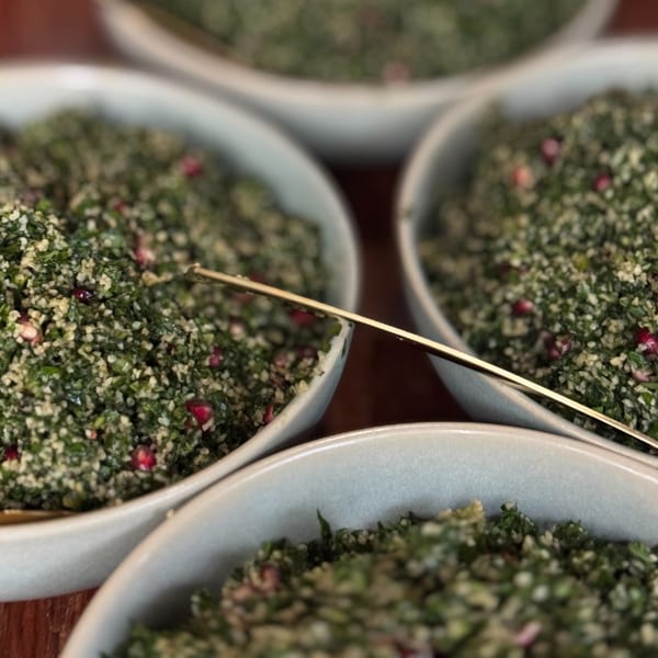 Close-up of multiple bowls filled with vibrant green tabbouleh salad, garnished with red pomegranate seeds.