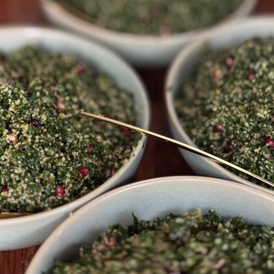 Close-up of multiple bowls filled with vibrant green tabbouleh salad, garnished with red pomegranate seeds.