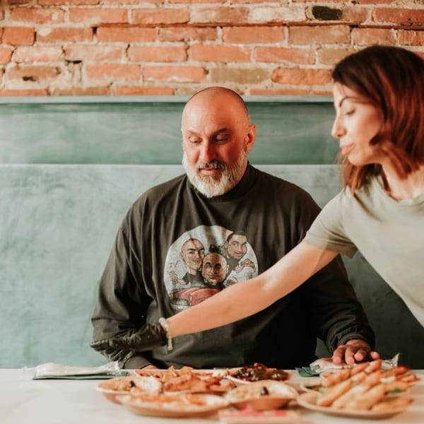 A server in a black glove places a plate of Middle Eastern food in front of a man.
