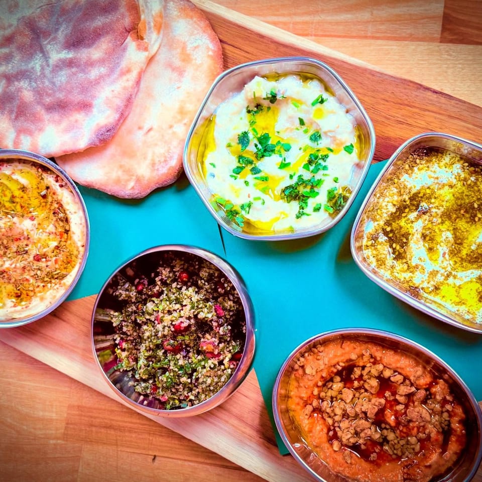 A vibrant spread of Middle Eastern dips and salads, including hummus, baba ghanoush, and tabbouleh, with pita bread.