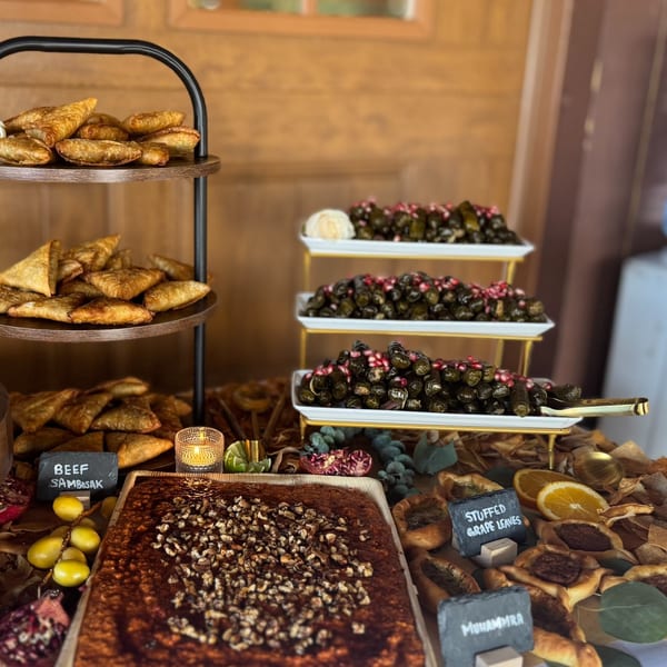 A buffet table laden with Middle Eastern dishes, including sambusak, stuffed grape leaves, and muhammara.