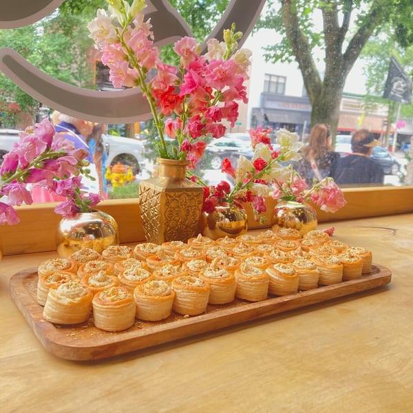 A wooden tray filled with vol-au-vents, topped with creamy filling and nuts, on a wooden table.