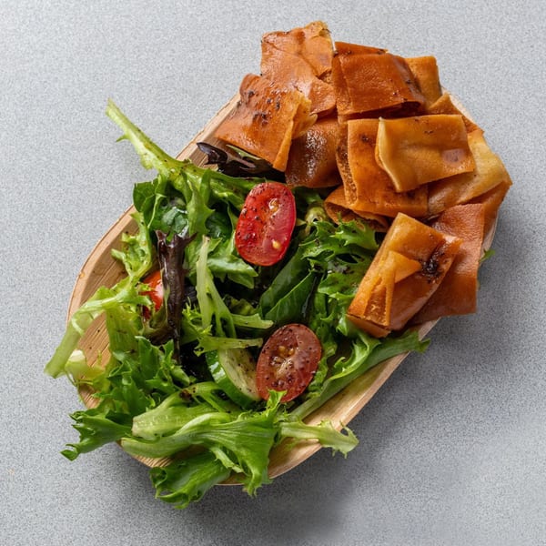 A wooden bowl of fresh green salad with cherry tomatoes and crispy fried pita bread.