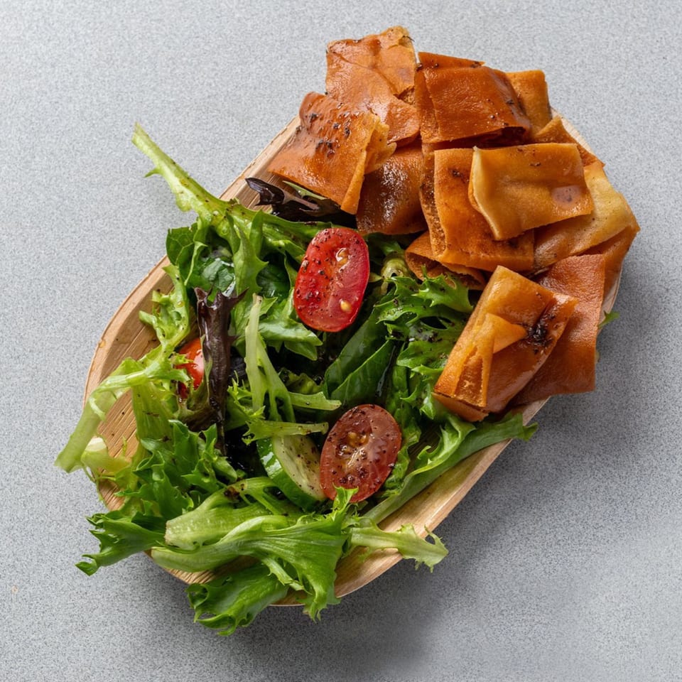 A wooden bowl of fresh green salad with cherry tomatoes and crispy fried pita bread.