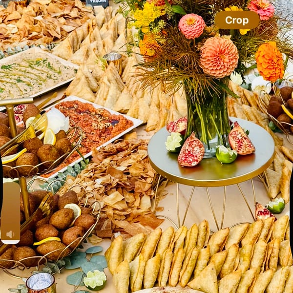 A buffet table laden with Middle Eastern appetizers, including kibbeh, pita chips, and pastries, with floral decor.