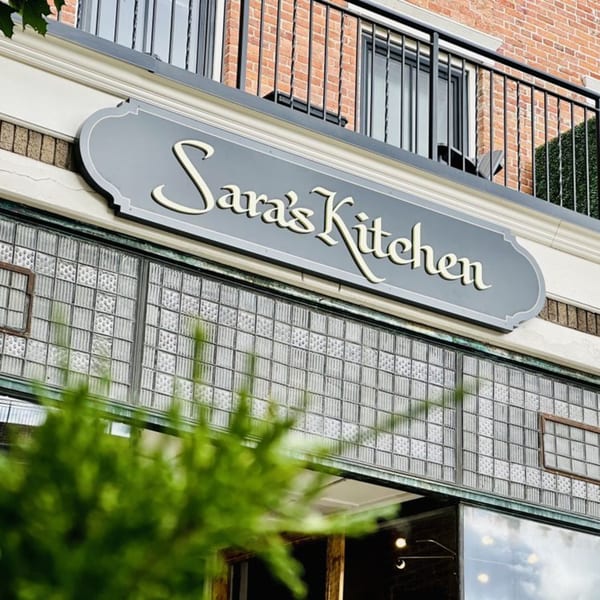 The Sara's Kitchen sign, with glass block windows and a brick building facade in the background.