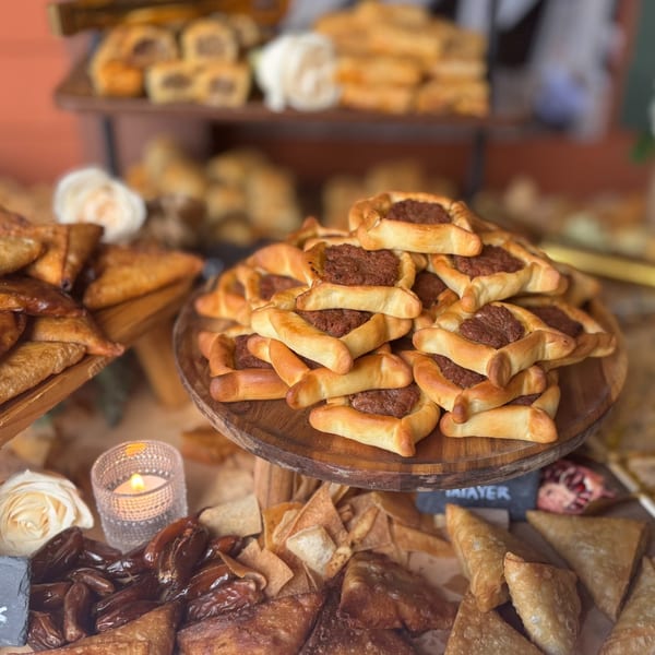A wooden display of savory pastries, including meat-filled fatayer and fried samosas, with dates and a candle.
